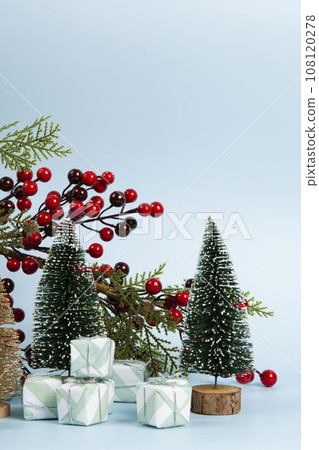Composition with colorful gifts, a branch of holly with its red berries and christmas tree against a luminous sky-blue background. 108120278