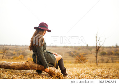 Beautiful stylish girl walks in the autumn park. The girl is dressed in a green coat and a red hat. 108120284