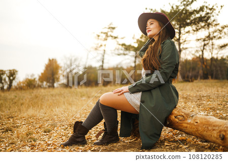 Beautiful stylish girl walks in the autumn park. The girl is dressed in a green coat and a red hat. 108120285