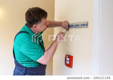 A worker screws on a sign with room numbers in a hotel 108121149
