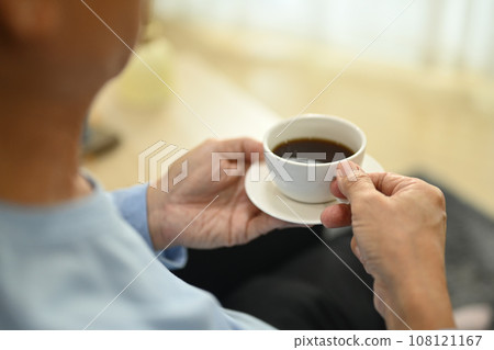 Pleased elderly man relaxing on armchair and drinking coffee in living room Pleased elderly man relaxing on armchair and drinking coffee in living room 108121167