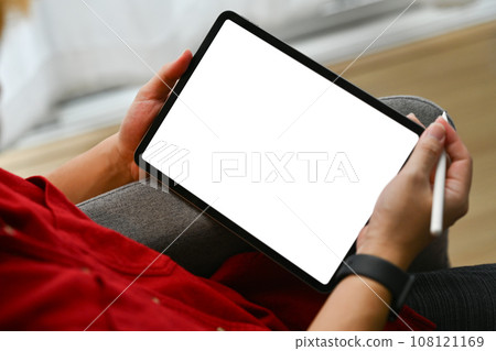 Close up shot young man hands holding digital tablet with blank screen sitting on couch at home Close up shot young man hands holding digital tablet with blank screen sitting on couch at home 108121169