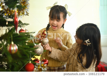 Adorable girls decorating Christmas tree and enjoying preparing winter holidays at home 108121170