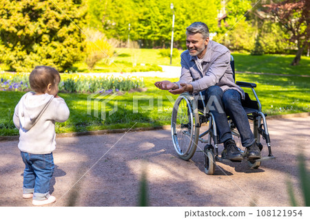 Dad on wheelchair playing with his little son in the park Dad on wheelchair playing with his little son in the park 108121954