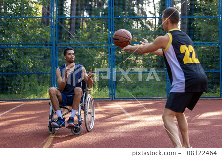 Wheelchair athlete and friend finding joy in outdoor basketball. Wheelchair athlete and friend finding joy in outdoor basketball. 108122464