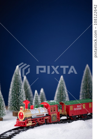 Toy locomotive on railway in the snow with Christmas tree. Christmas and New Year background. Creative winter Christmas composition. Toy locomotive on railway in the snow with Christmas tree. Christmas and New Year background. Creative winter Christmas composition. 108122642