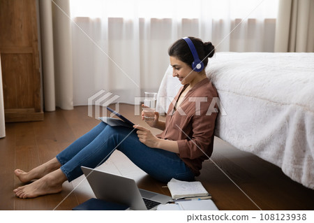 Indian woman in headphones holding glass of water, studying online Indian woman in headphones holding glass of water, studying online 108123938