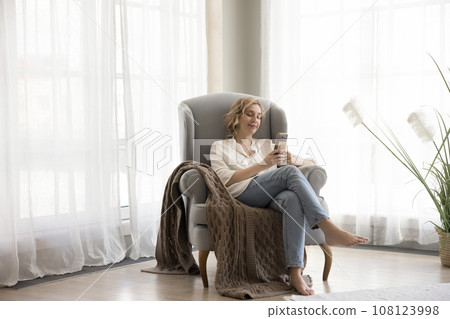 Carefree woman relaxing at home with smartphone 108123998