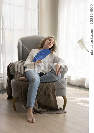 Tired woman sits on armchair suffer from high temperature inside Tired woman sits on armchair suffer from high temperature inside 108124000