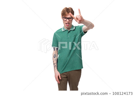 portrait of a young confident stylish red-haired guy in a green t-shirt and brown pants 108124173