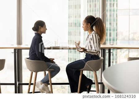 Positive office friends women talking at office large city window Positive office friends women talking at office large city window 108124310