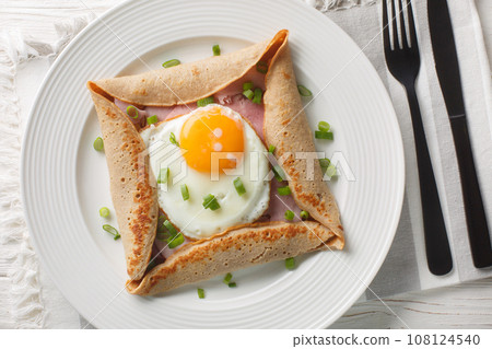 Breton crepe, Savory Buckwheat Galettes Bretonnes with fried egg, cheese, ham closeup on the plate. Horizontal top view Breton crepe, Savory Buckwheat Galettes Bretonnes with fried egg, cheese, ham closeup on the plate. Horizontal top view 108124540