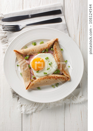 Homemade buckwheat crepe galette with egg, ham and green onion closeup on the plate. Vertical top view Homemade buckwheat crepe galette with egg, ham and green onion closeup on the plate. Vertical top view 108124544