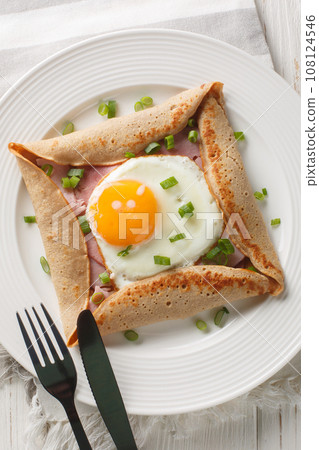 Buckwheat crepe galette with ham and egg for tasty healthy breakfast closeup on the plate on the table. Vertical top view 108124546