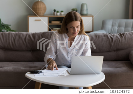 Satisfied pretty millennial laptop user woman checking domestic paper documents Satisfied pretty millennial laptop user woman checking domestic paper documents 108124572