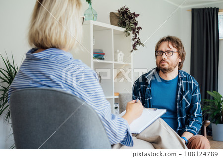 Depressed male patient having psychotherapy session with counselor at mental health clinic. Man with emotional problems consulting professional therapist i comfy office. Psychological help service. 108124789