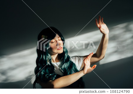 Beautiful tender woman with long dark green hair and closed eyes catching light in ray of sun from window. Attractive fantasy girl, Young elven princess style. A gentle image. Feelings and emotions. 108124790