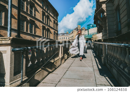 Outdoor autumn portrait of young elegant fashionable woman wearing trendy sunglasses, gray color coat, black jeans and turtleneck walking on street of European city in sunny day. street style fashion. Outdoor autumn portrait of young elegant fashionable woman wearing trendy sunglasses, gray color coat, black jeans and turtleneck walking on street of European city in sunny day. street style fashion. 108124838