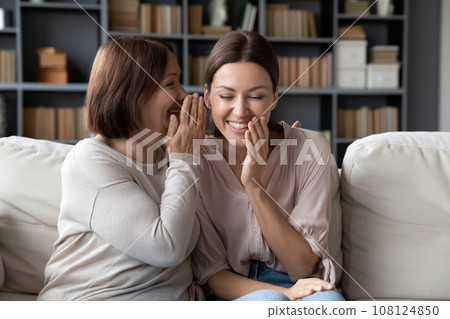 Elderly mother telling on ear to adult daughter a secret Elderly mother telling on ear to adult daughter a secret 108124850