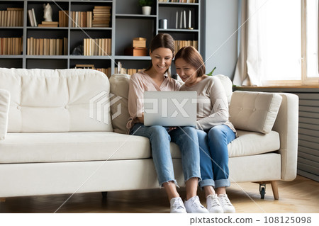 Grownup daughter holds on lap laptop explain mother new apps Grownup daughter holds on lap laptop explain mother new apps 108125098