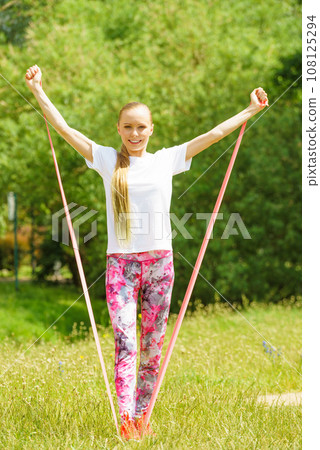 Girl doing exercises outdoor, using resistance fit band. 108125294