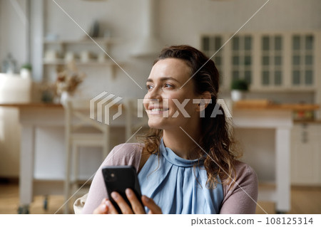 Smiling thoughtful young woman holding mobile phone 108125314
