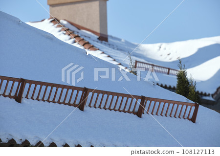 Snow guard for safety in winter on house roof top covered with ceramic shingles. Tiled covering of building 108127113