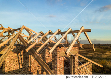 Private residential house with wooden roof frame structure under construction. Unfinished brick building under development. 108127180