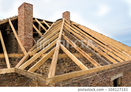 Private residential house with wooden roof frame structure under construction. Unfinished brick building under development. 108127181
