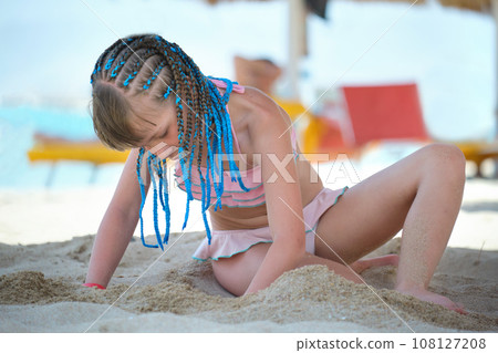 Pretty child girl in bikini swimsuit playing with sand in umbrella shadow during summer tropical vacation 108127208