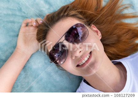 Portrait of young teenage girl in sunglasses laying down on blue cloth background. 108127209