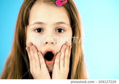 Portrait of surprised child girl holding hands to her face isolated on blue background. Portrait of surprised child girl holding hands to her face isolated on blue background. 108127220