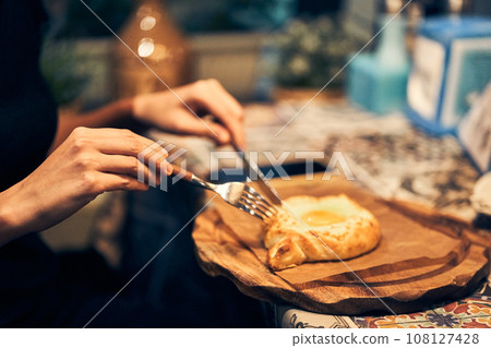 Women's hands cut baked bread with cheese and egg filling with a knife. Khachapuri in Adjarian is a traditional dish of Georgian cuisine. High quality photo 108127428