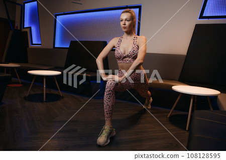 Sports. Woman at the gym doing stretching exercises and smiling on the floor. Beautiful slim fitness trainer on a reformer. Fitness, sport, training and lifestyle concept. 108128595