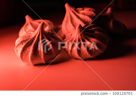 Four meringue cookies in red light on a dark background. 108128701