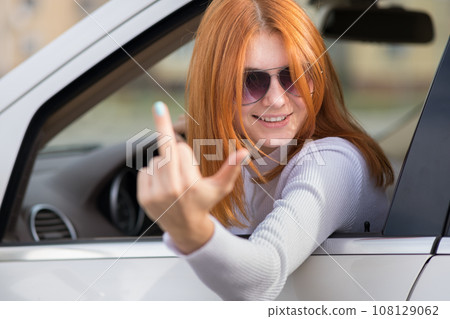 Pissed off displeased angry aggressive woman driving a car shouting at someone with middle finger gesture. 108129062