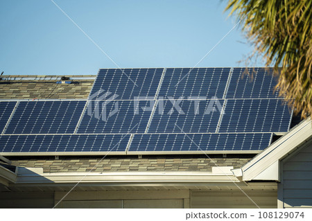 Ordinary residential house in USA with roof covered with solar panels for producing of clean ecological electricity in suburban rural area. Concept of investing in autonomous home for energy saving Ordinary residential house in USA with roof covered with solar panels for producing of clean ecological electricity in suburban rural area. Concept of investing in autonomous home for energy saving 108129074