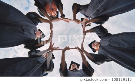 College graduates in black robes make the shape of a square from their hands. 108129113