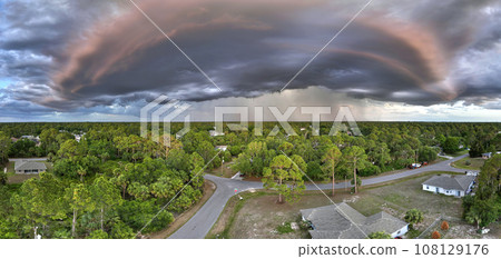 Landscape of dark ominous clouds forming on stormy sky during heavy thunderstorm over rural town area at sunset 108129176