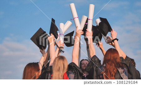 Graduates connect diplomas and caps on a sunny day. Graduates connect diplomas and caps on a sunny day. 108129184