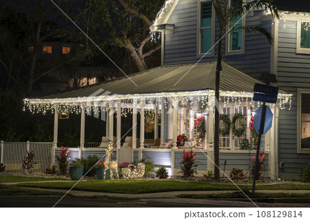 House front yard with big porch brightly illuminated with christmas decorations. Outside decor of florida family home for winter holidays House front yard with big porch brightly illuminated with christmas decorations. Outside decor of florida family home for winter holidays 108129814