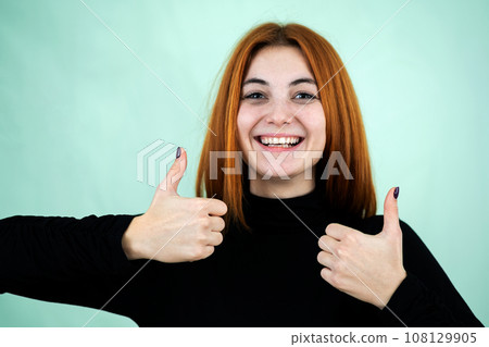 Funny pretty redhead girl showing thumbs up sign with her fingers. 108129905