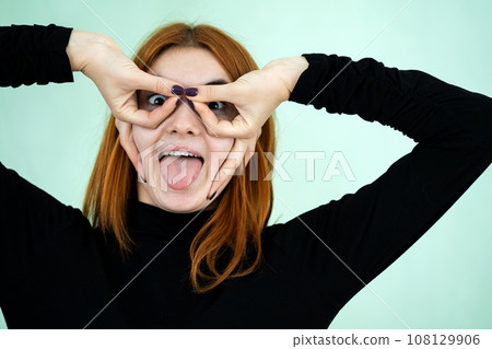 Funny pretty redhead girl showing glasses sign with her fingers. 108129906
