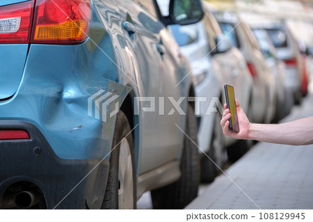 Driver hands taking photo on mobile phone camera after vehicle collision on street side for emergency service after car accident. Road safety and insurance concept 108129945