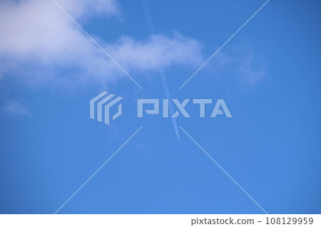 Distant passenger jet plane flying on high altitude on blue sky with white clouds leaving smoke trace of contrail behind. Air traveling concept. Distant passenger jet plane flying on high altitude on blue sky with white clouds leaving smoke trace of contrail behind. Air traveling concept. 108129959