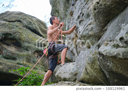 Determined climber clambering up steep wall of rocky mountain. Sportsman overcoming difficult route. Engaging in extreme sports and rock climbing hobby concept. 108129961