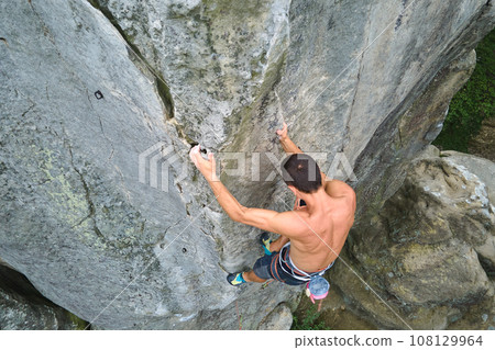 Determined climber clambering up steep wall of rocky mountain. Sportsman overcoming difficult route. Engaging in extreme sports and rock climbing hobby concept. 108129964