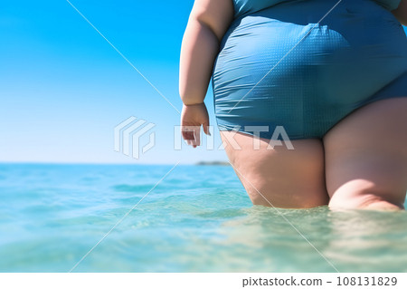 rear view of a plump girl in a closed turquoise swimsuit who enters the ocean water rear view of a plump girl in a closed turquoise swimsuit who enters the ocean water 108131829