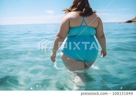 plump woman in a closed turquoise swimsuit enters the ocean water to swim plump woman in a closed turquoise swimsuit enters the ocean water to swim 108131849