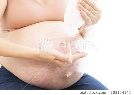 A woman's hand applying cream to her belly with stretch marks and her pregnant belly 108134143